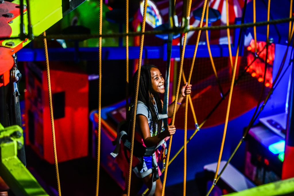 밝고 다채로운 요소에 둘러싸인 실내에서 로프 장애물 코스를 탐색하며 웃고 있는 소녀.