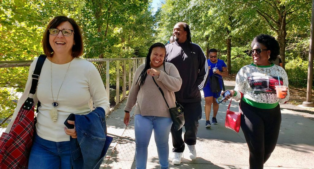 화창한 날 야외에서 나무와 금속 난간이 있는 길로 둘러싸인 한 무리의 사람들.