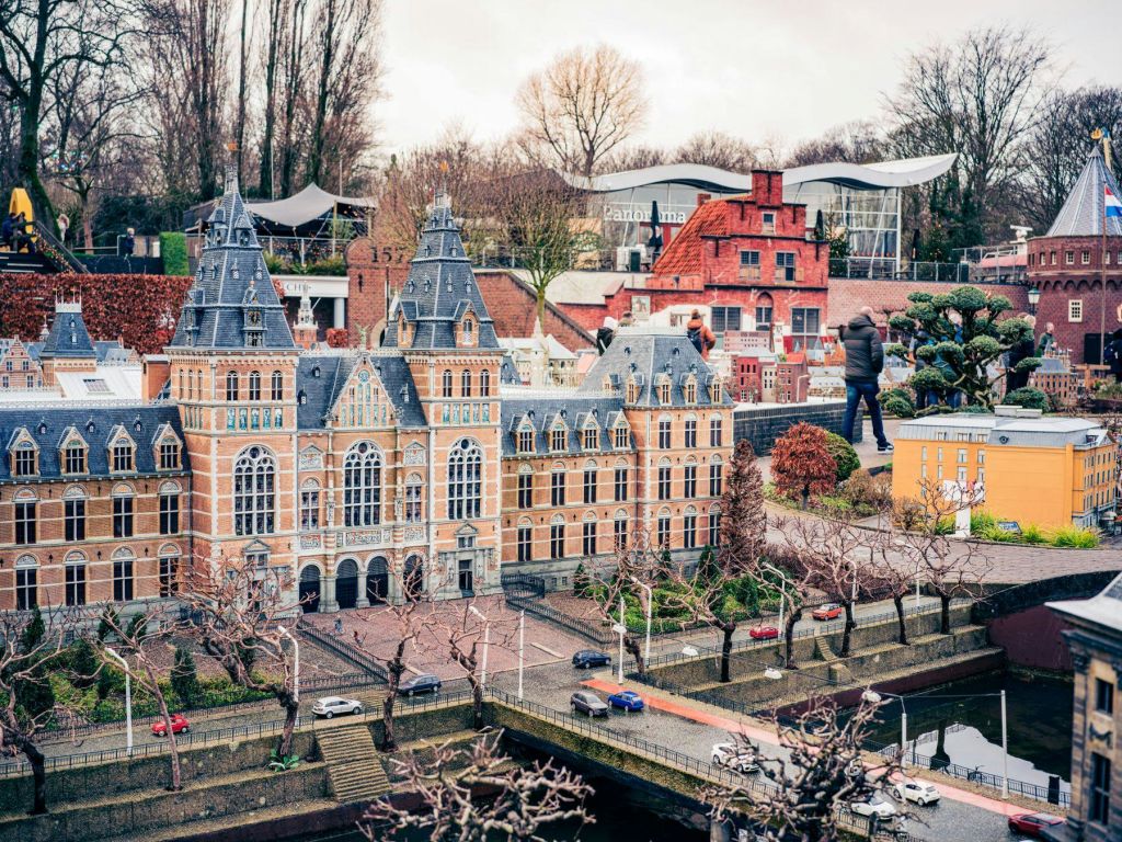 한 사람이 커다랗고 화려한 구조물과 주변 주택 등 세부적인 미니어처 건물 옆에 서 있으며, 근처에 맨발의 나무와 모형 자동차가 있습니다.