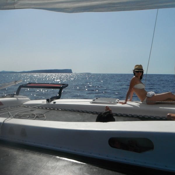 모자와 수영복을 입은 사람이 잔잔한 바닷물을 배경으로 맑은 하늘 아래 요트에서 휴식을 취하고 있습니다.