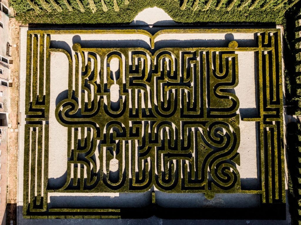 녹색과 베이지색으로 대칭적으로 "BORGES" 를 철자하는 복잡한 헤지 패턴의 미로를 공중에서 볼 수 있습니다.