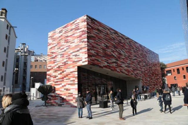 맑은 날 현대적인 빨간색과 분홍색 무늬의 벽돌 건물 근처에 서 있는 사람들.