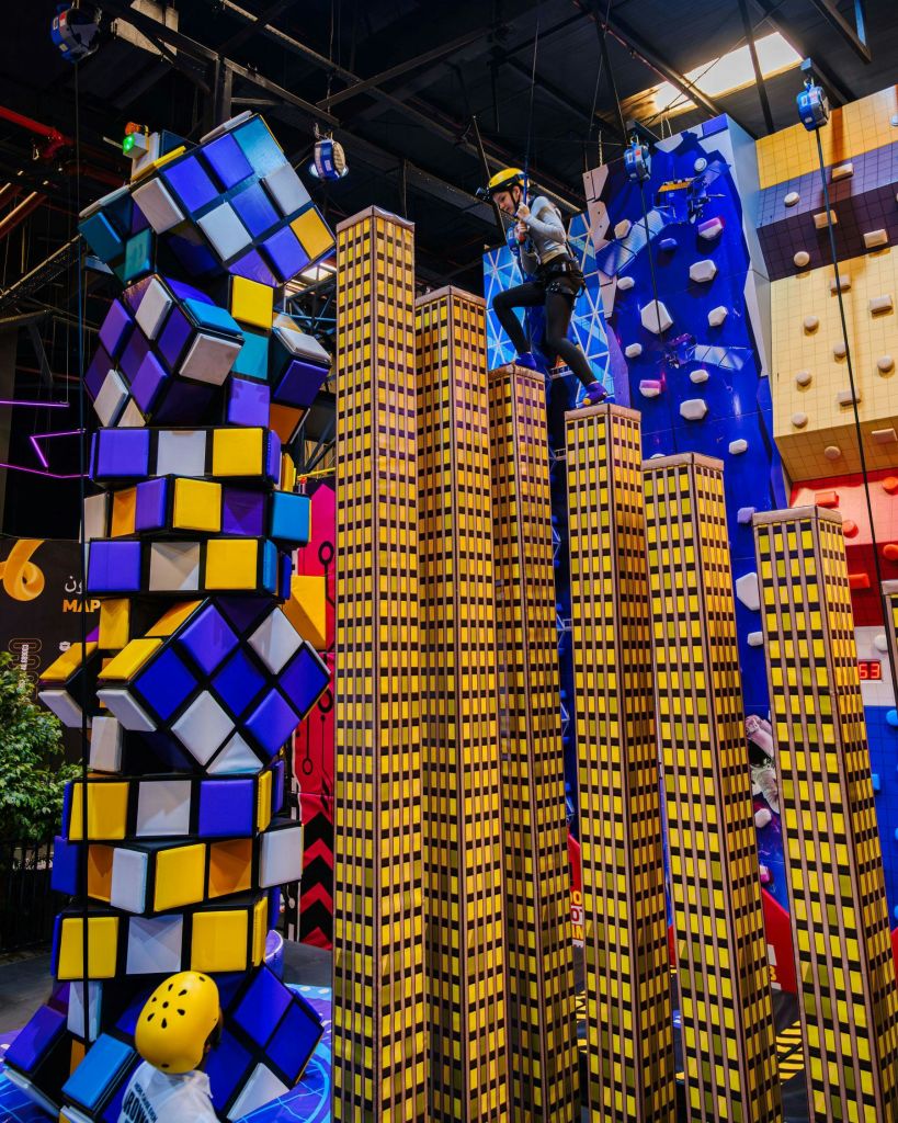 실내 등반 액티비티 센터에서 등산 장비를 착용한 사람이 높은 인공 고층 건물 꼭대기에 서 있습니다.