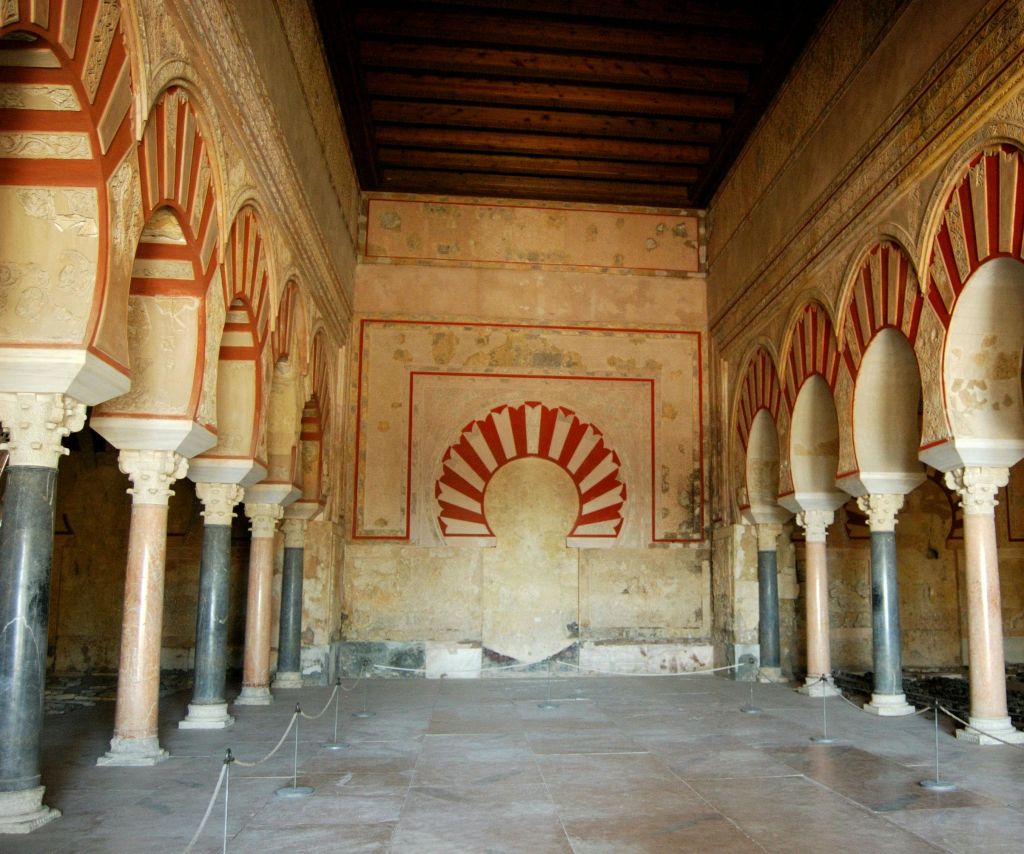 빨간색과 흰색 줄무늬 아치, 디테일한 벽 조각, 아치를 받치고 있는 줄무늬 기둥이 있는 화려한 홀입니다.