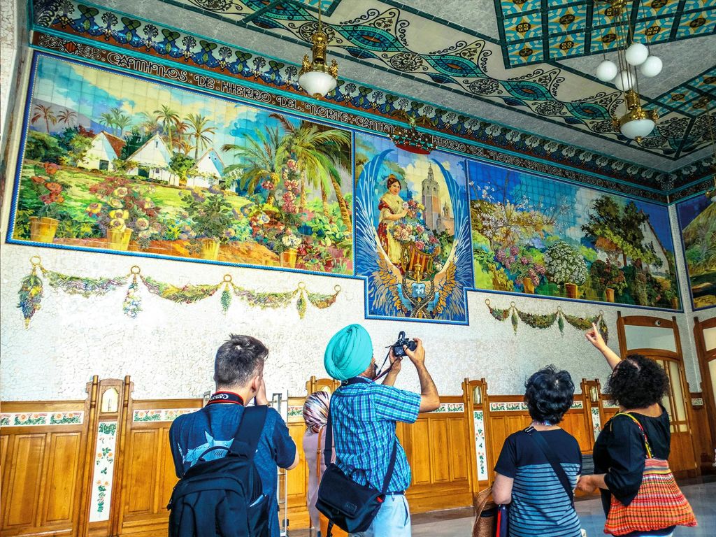 세 사람은 열대 풍경을 묘사한 크고 생동감 넘치는 벽화와 장식된 방에서 꽃을 든 한 여성을 감상합니다.