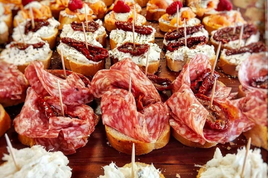 작은 빵 조각에 고기, 치즈, 말린 토마토, 장식품을 얹은 다양한 전채의 클로즈업.