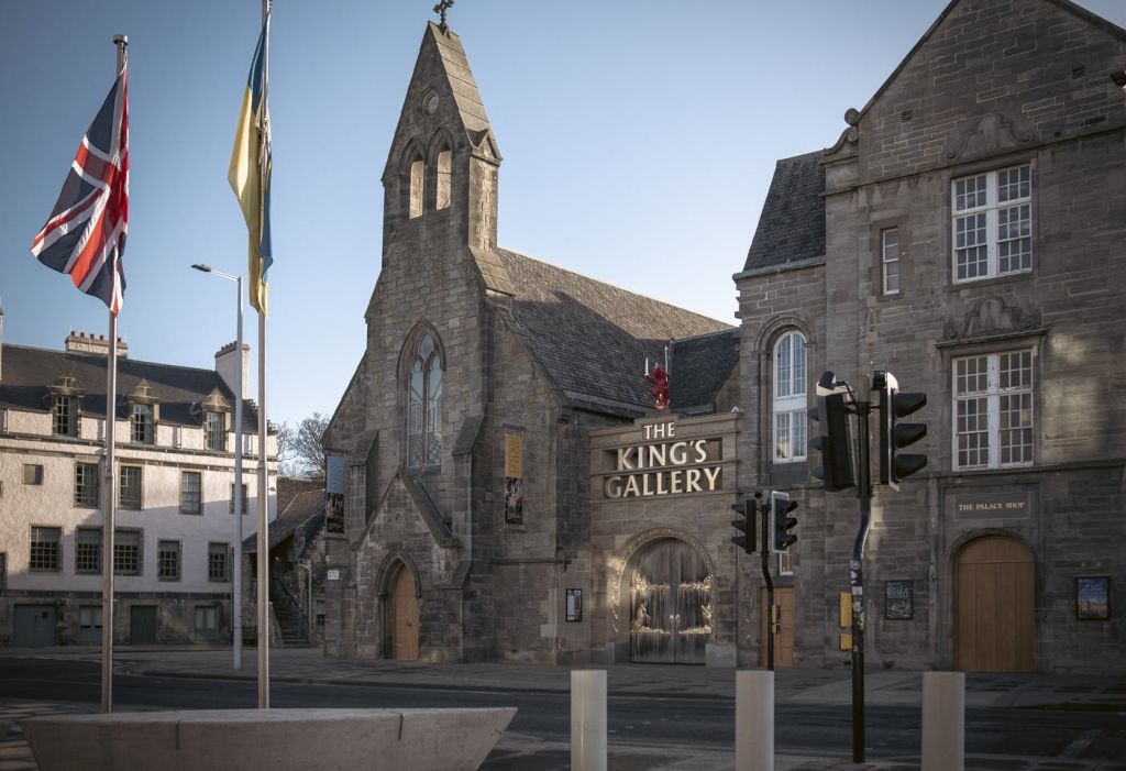 "왕의 갤러리" 라고 표시된 고딕 양식의 건축물이 있는 석조 건물. 전경에 깃발과 신호등이 보입니다.