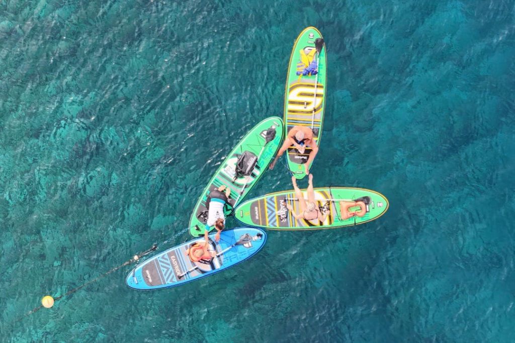 청록색의 맑은 물 위에 뭉친 패들보드에서 휴식을 취하는 네 명의 사람들.