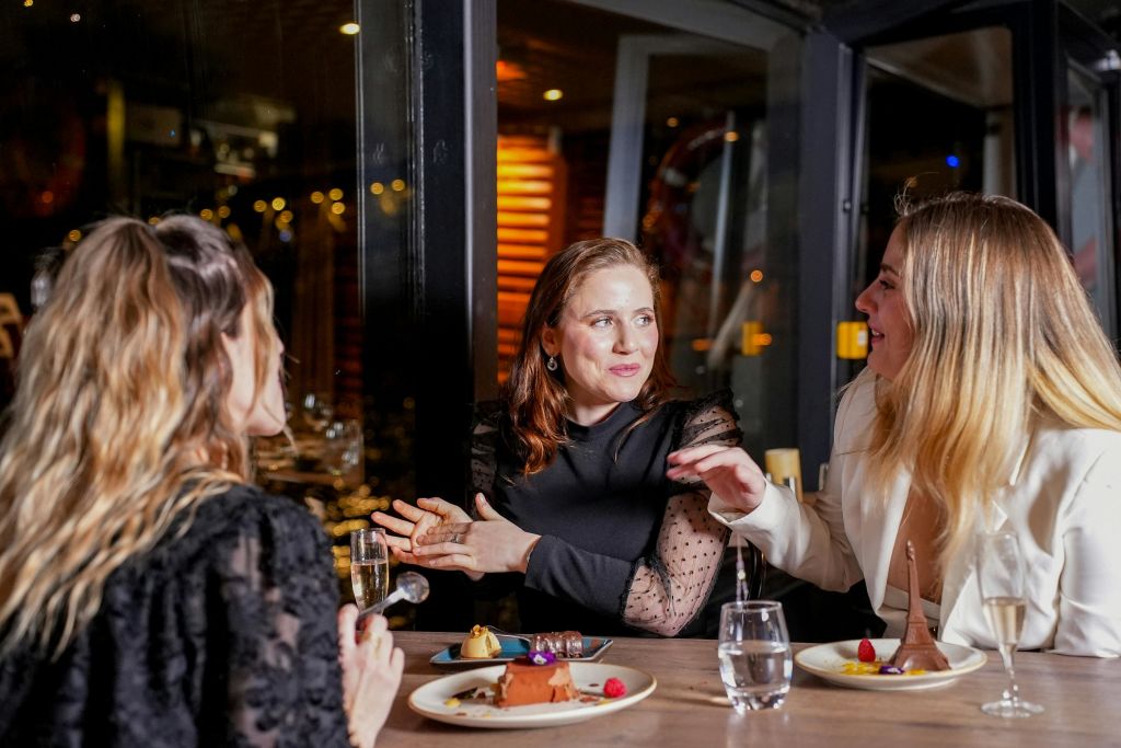 두 여성이 레스토랑의 테이블에 앉아 대화를 나누고 있으며, 디저트 접시와 유리잔을 앞에 두고 있습니다.