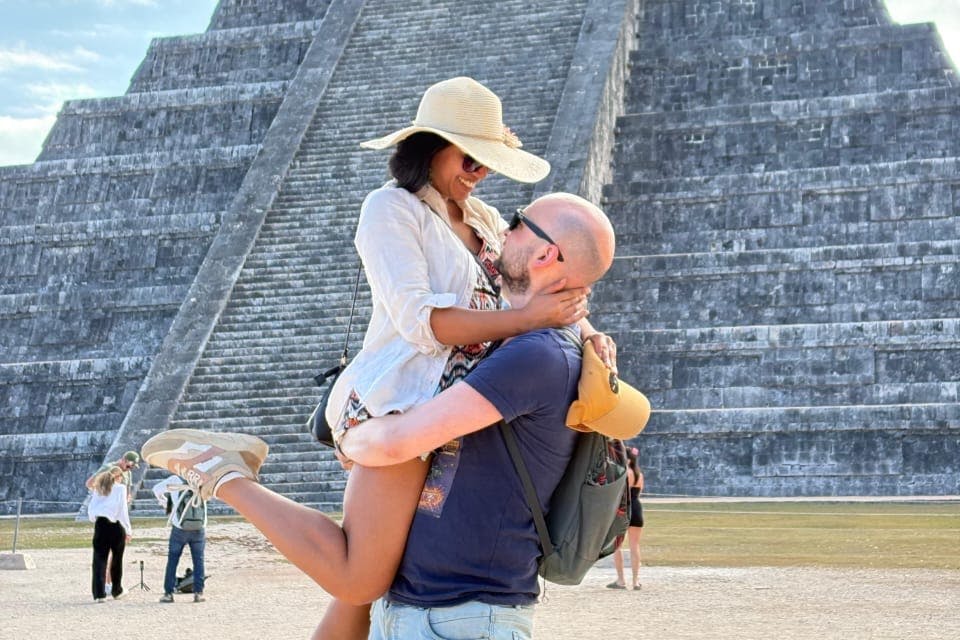 화창한 날씨에 커다란 석조 피라미드 앞에서 한 커플이 다른 방문객을 배경으로 행복하게 포옹하고 있습니다.