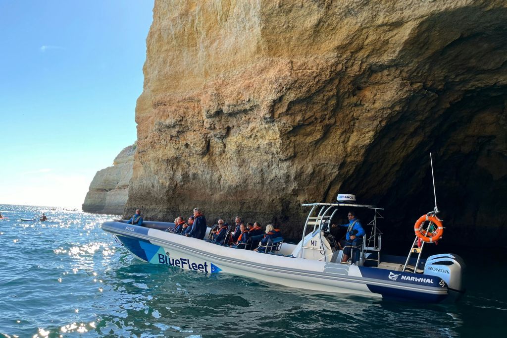 화창한 날 바위 해안 동굴 근처에서 구명조끼를 입은 승객과 함께 블루플리트 (BlueFleet) 라는 이름의 보트.