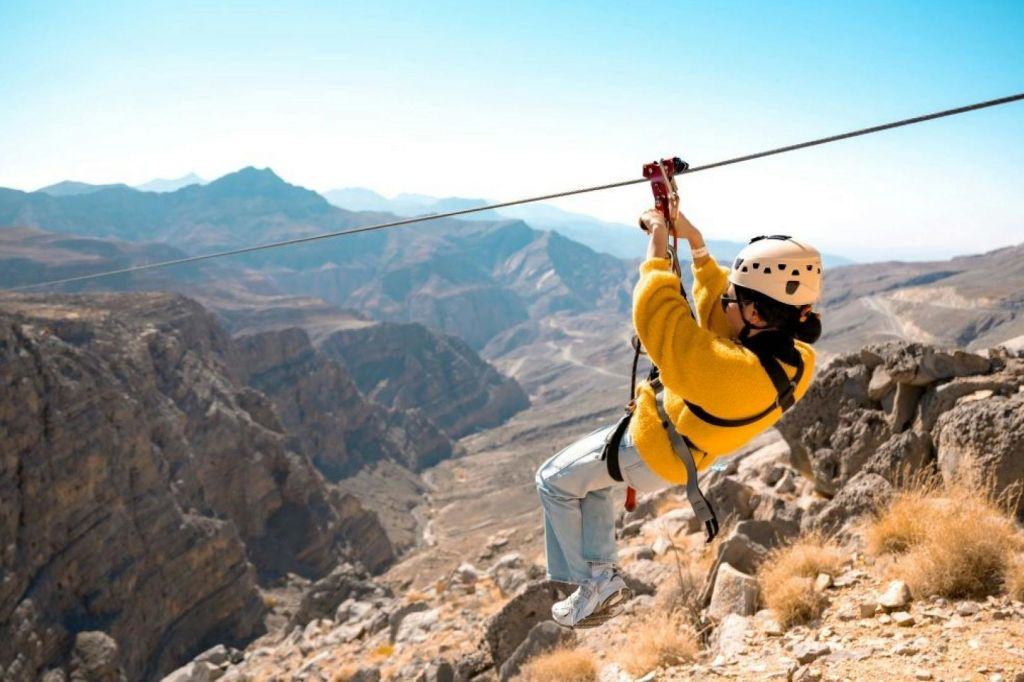 맑고 푸른 하늘 아래 험준한 산악 지형 위에서 노란 재킷과 헬멧을 착용하고 있는 사람.