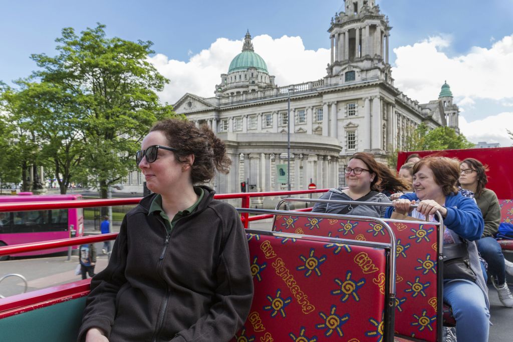 부분적으로 흐린 하늘 아래 돔과 기둥이 있는 유서 깊은 건물 앞에 오픈탑 도시 관광 버스를 탄 관광객.