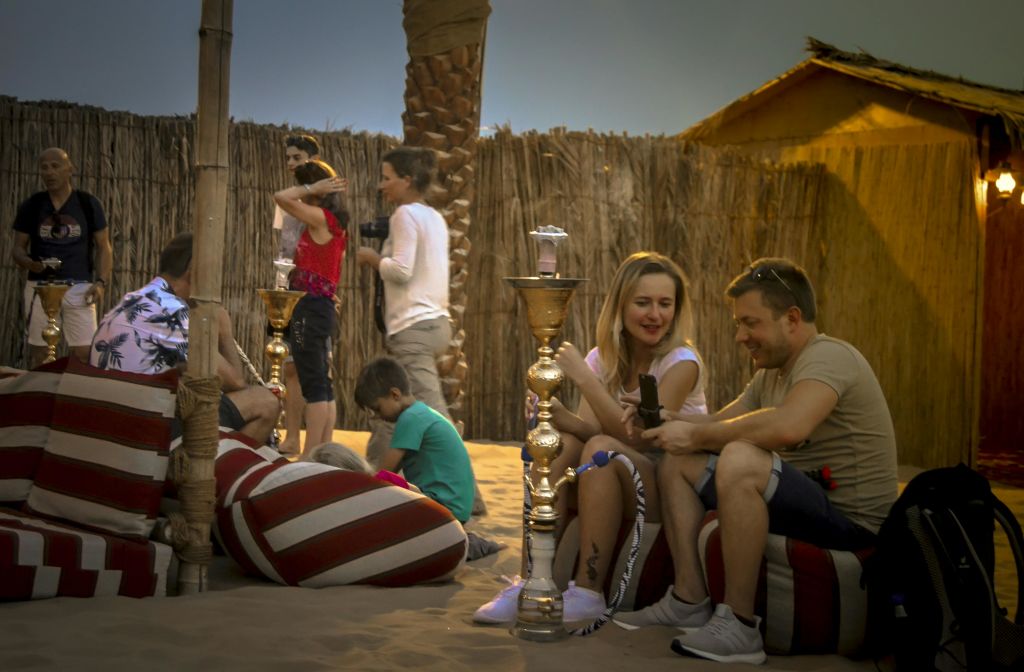 후카와 나무 울타리를 배경으로 모래사장의 줄무늬 쿠션에서 휴식을 취하는 사람들.