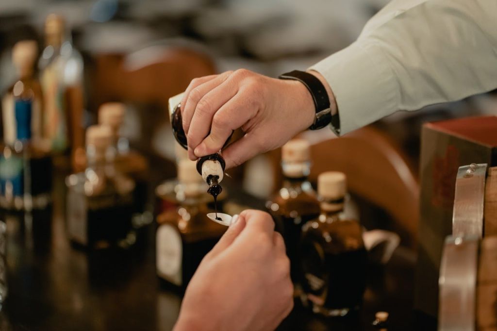 한 사람이 작은 병에서 나온 액체를 다른 사람이 들고 있는 숟가락에 붓고, 여러 병이 배경에 보입니다.