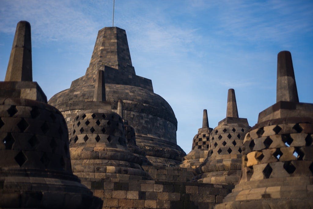 인도네시아의 보로부두르 사원을 보여주는 석조 스투파와 맑고 푸른 하늘 아래 보이는 커다란 중앙 구조물.