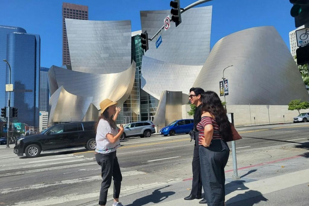 맑고 푸른 하늘 아래 모던하고 금속으로 마감된 건물 근처의 길 모퉁이에 세 사람이 서 있습니다.