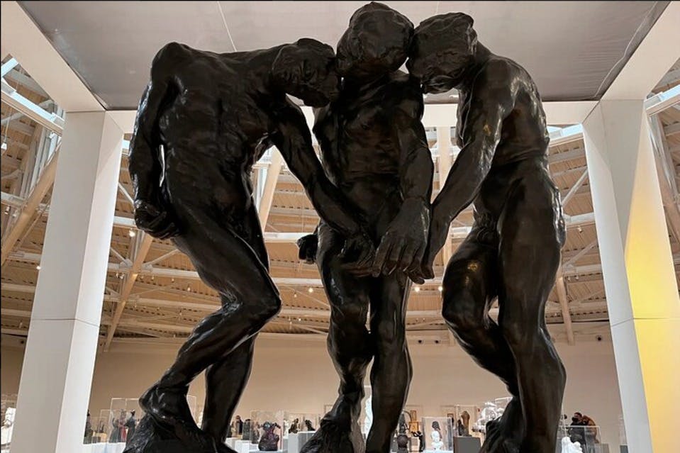 조명이 밝은 박물관 갤러리에 얽히고설킨 어두운 청동 동상 세 개가 전시되어 있습니다.