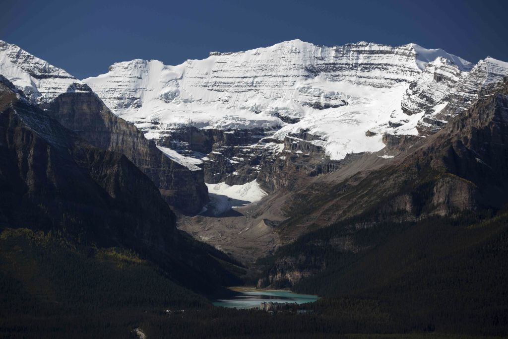 험준한 절벽이 있는 눈 덮인 산이 청록색 호수를 둘러싸고 있으며, 맑고 푸른 하늘 아래 푸른 계곡이 펼쳐져 있습니다.