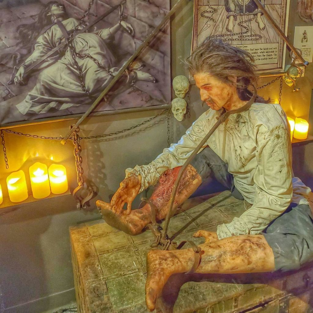 촛불, 쇠사슬, 고문 장면을 묘사한 음침한 예술품으로 둘러싸인 역사적 구속 속에 마네킹을 전시합니다.