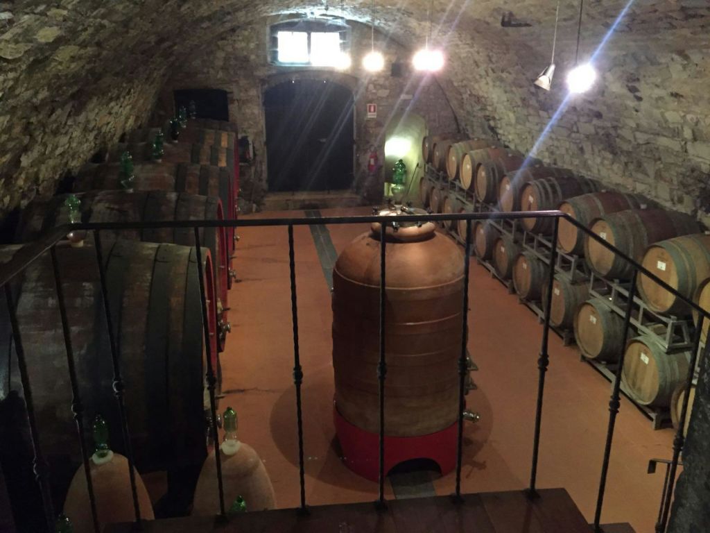 돌담, 나무 통, 중앙에 커다란 점토 통이 있는 조명이 희미한 와인 저장고.