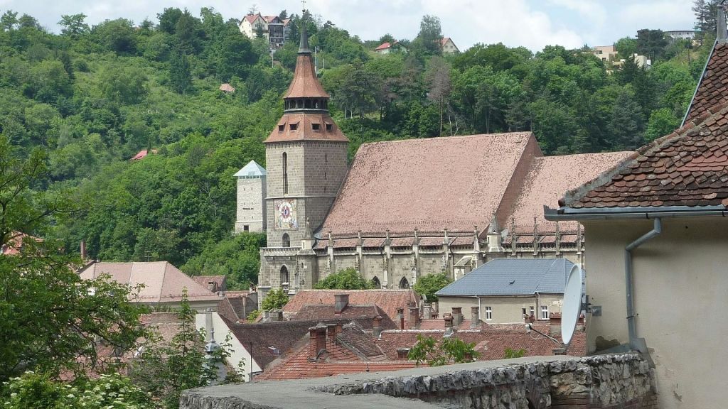 붉은 기와 지붕과 종탑이 있는 대형 석조 교회는 나무로 덮인 언덕과 비슷한 지붕의 건물로 둘러싸여 있습니다.