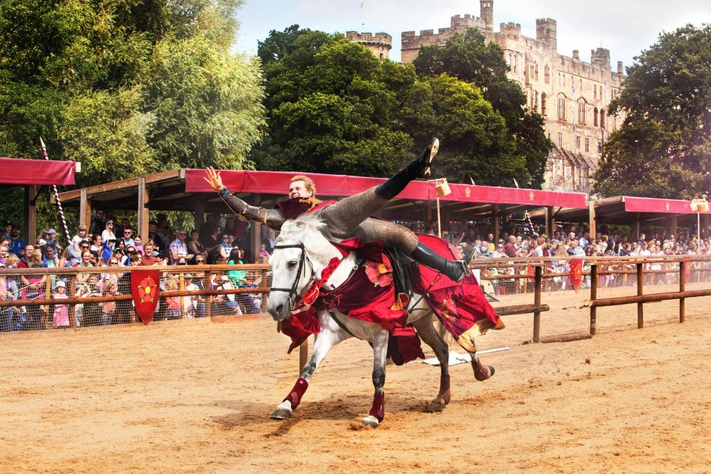 군중과 성을 배경으로 펼쳐지는 황홀한 쇼에서 백마를 타고 중세 복장의 균형을 맞추는 연주자.