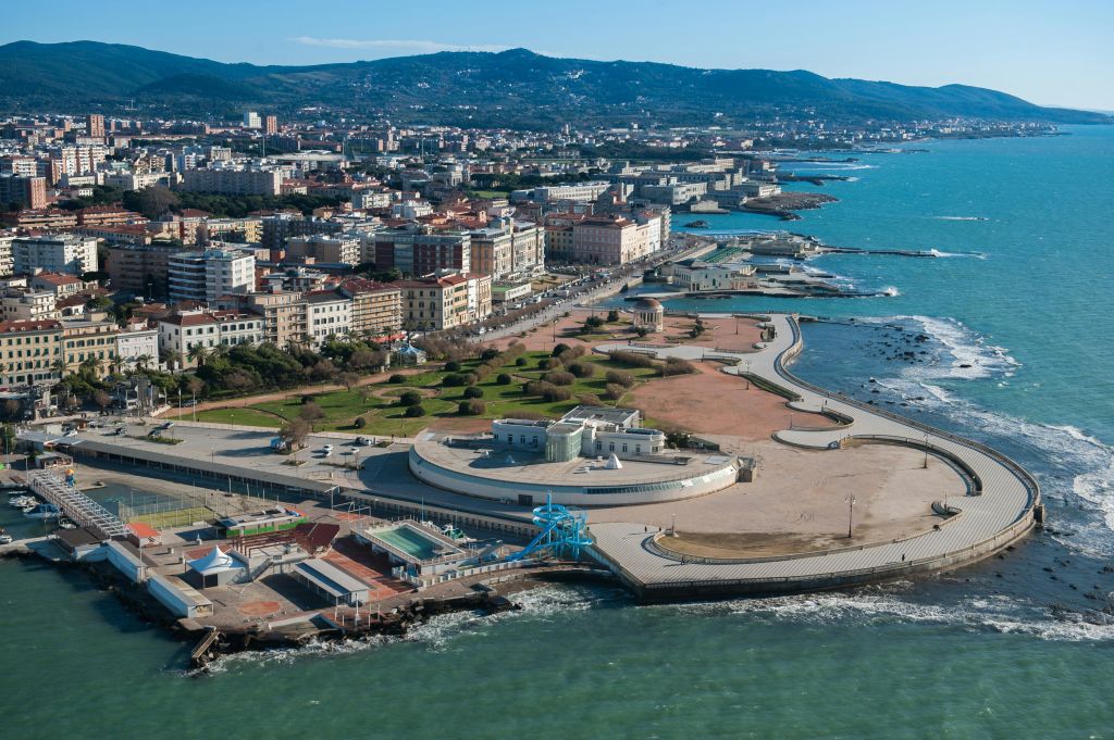 산책로로 둘러싸인 청록색 바다를 따라 건물, 도로, 공원, 해안선이 있는 해안 도시의 공중 전망.