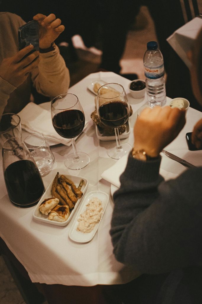 음식 접시, 레드 와인 2잔, 물병, 3명이 둘러앉은 테이블.