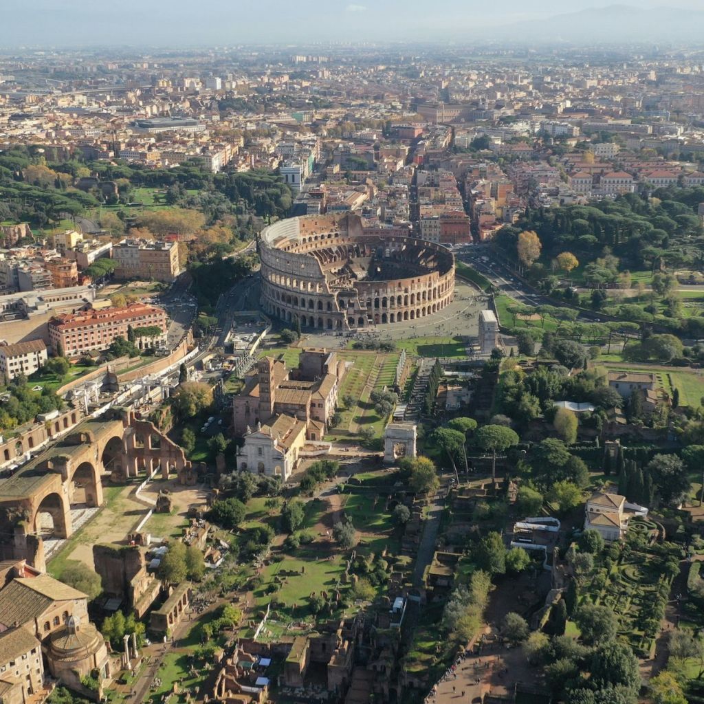 맑은 하늘 아래 도시 건물과 녹지로 둘러싸인 로마의 콜로세움의 공중 전망.