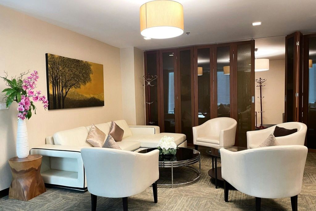 흰색 안락의자, 소파, 원형 커피 테이블, 부드러운 조명 아래 벽에 페인팅이 있는 현대적인 라운지 공간입니다.