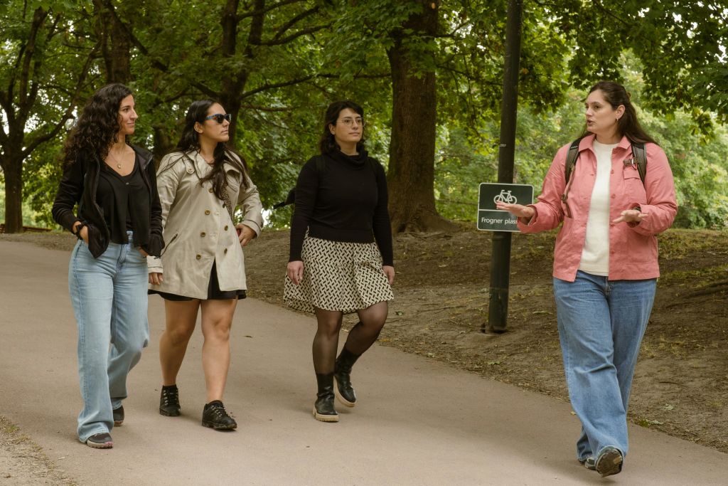 공원 길을 걷고 있는 세 명의 여성은 분홍색 재킷을 입고 나무와 간판을 배경으로 이야기를 나눕니다.