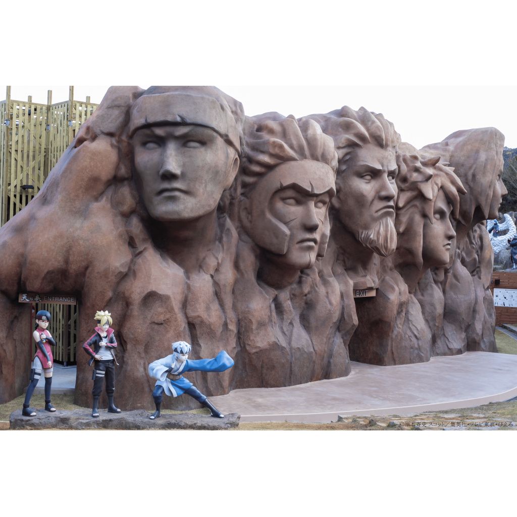 다섯 개의 조각된 얼굴이 있는 바위 지층 앞에 있는 실물 크기의 애니메이션 캐릭터 조각상 네 개.