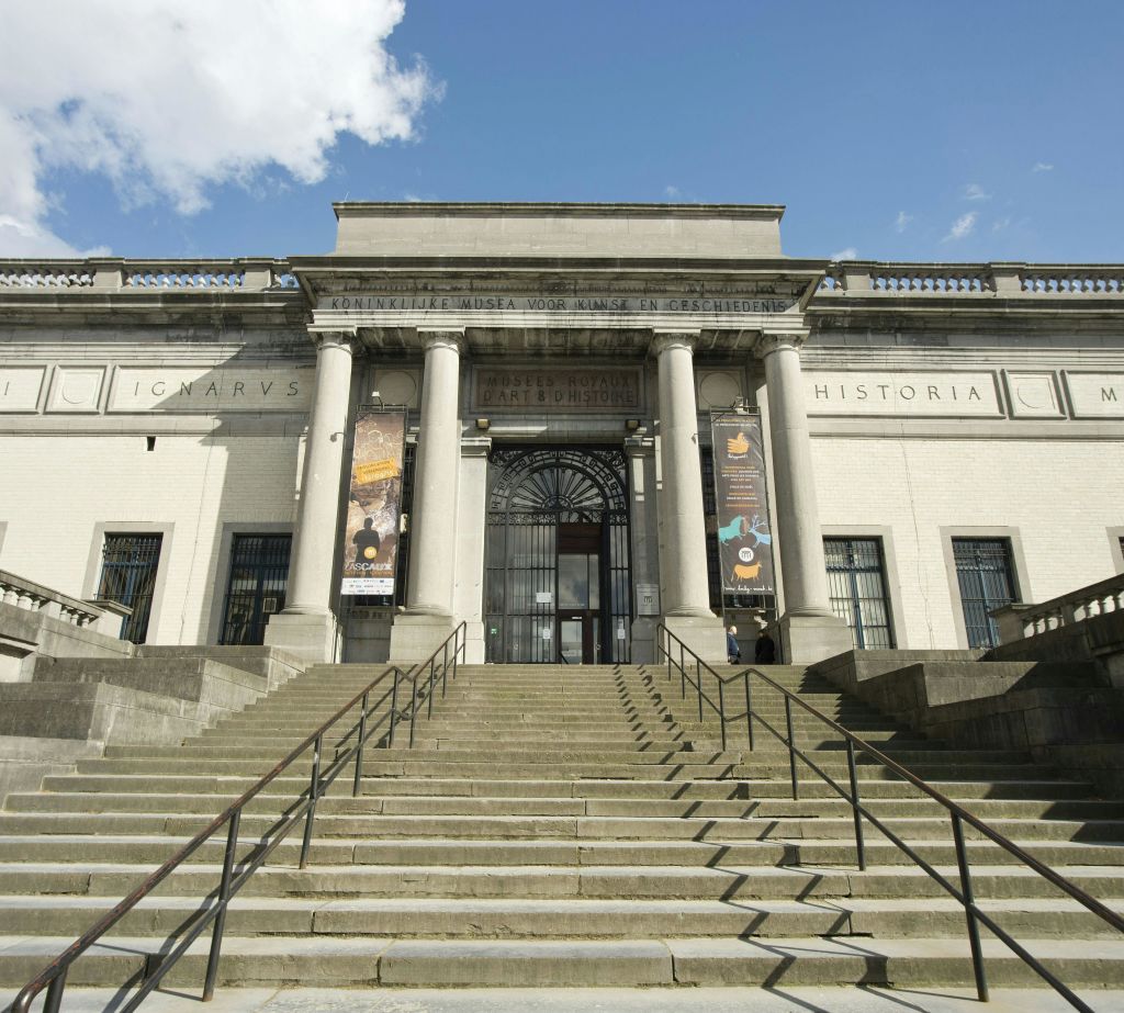 계단, 기둥, 현수막, 부분적으로 흐린 하늘 아래 장식된 아치형 통로가 있는 역사적인 건물의 웅장한 석조 입구.