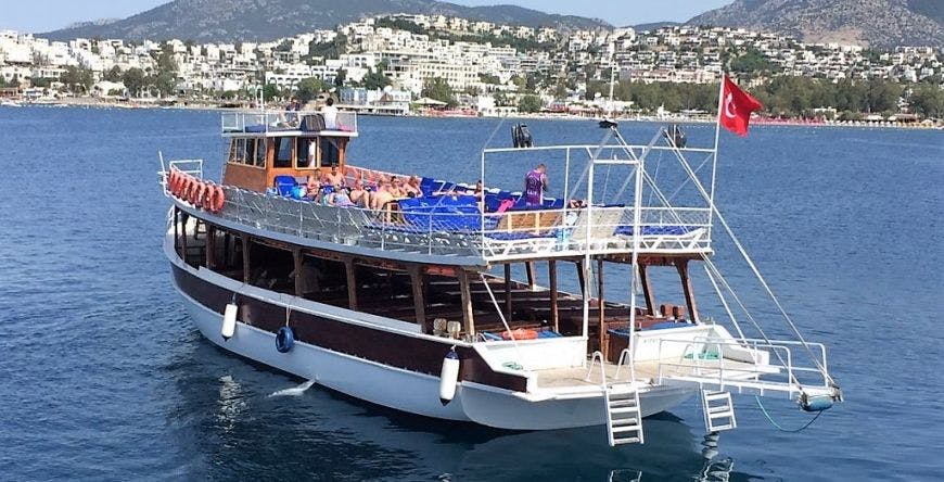 해안 마을과 언덕을 배경으로 푸른 만이 펼쳐진 데크에서 일광욕을 즐기는 목조 투어 보트입니다.