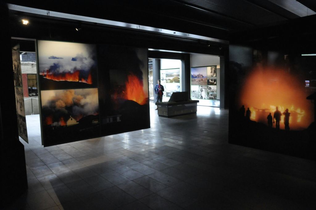 어두운 벽에 화산 폭발의 대형 사진을 전시하는 박물관 전시실. 한 사람이 배경에 서 있습니다.