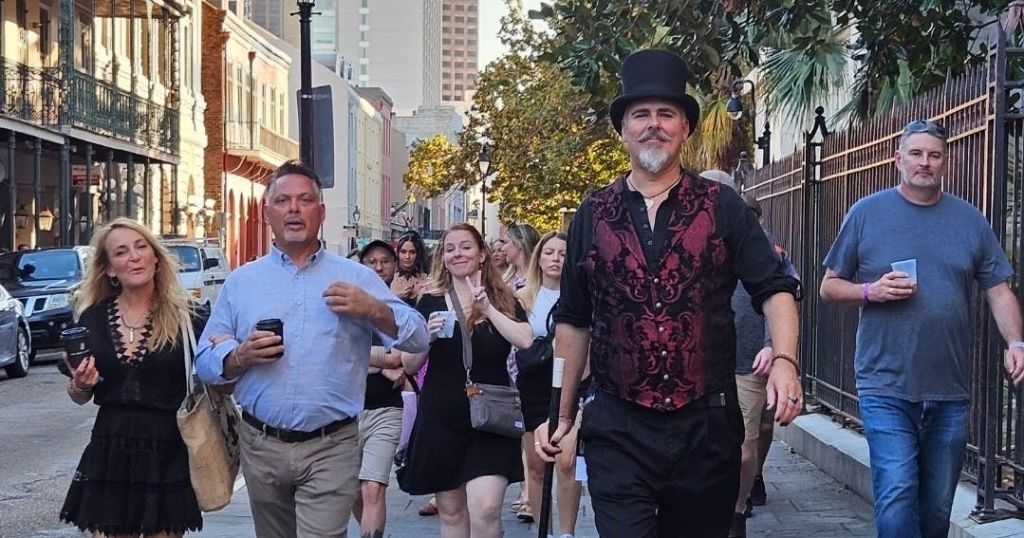 화창한 날 건물과 나무를 배경으로 한 도시 거리를 걷고 있는 한 무리의 사람들.