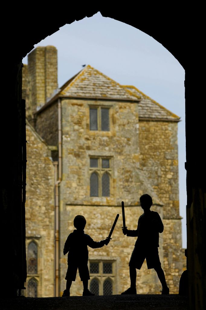 아치형 창문과 타일 지붕이 있는 오래된 석조 건물을 배경으로 장난감 검을 든 두 아이가 있었다.