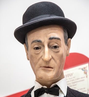 검은색 볼러 모자, 흰색 셔츠, 검은색 나비 넥타이, 정장을 착용하고 중성적인 표정을 짓는 왁스 피규어.