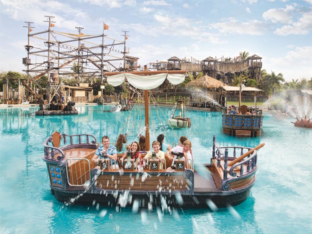 해적을 테마로 한 보트를 타는 어린이와 성인은 로프 코스를 배경으로 놀이 공원을 배경으로 물대포를 타고 다닙니다.