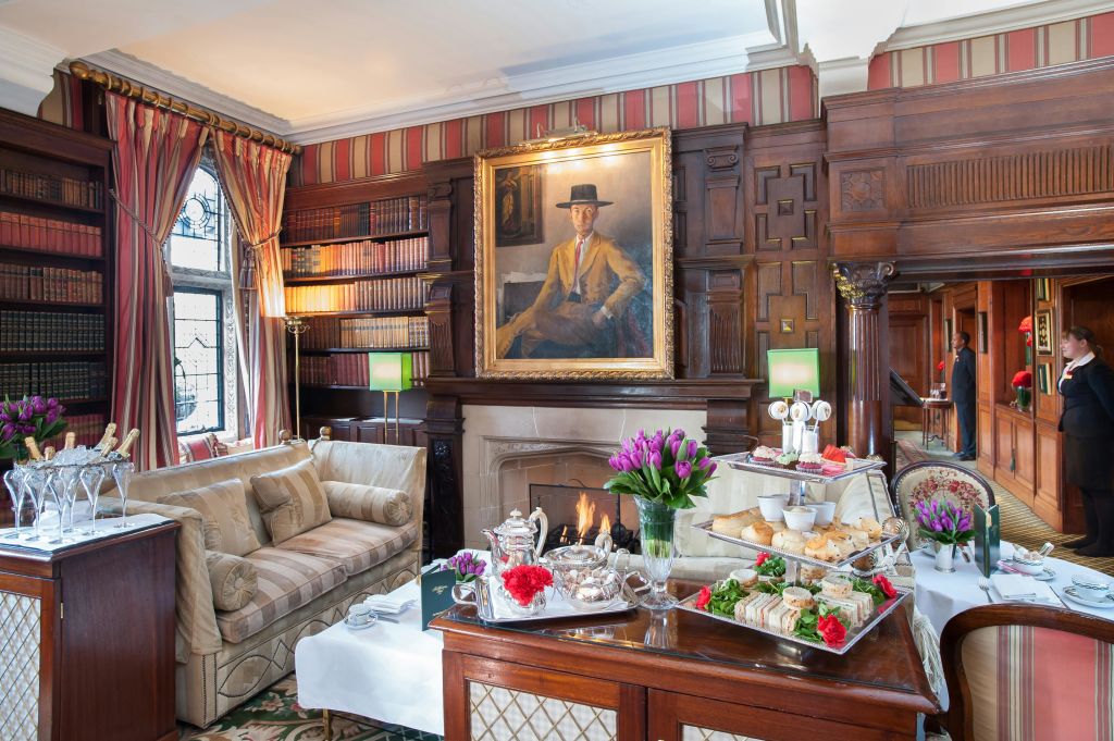 벽난로, 그 위에 그림, 책장, 아늑한 좌석, 애프터눈 티와 꽃이 놓인 테이블이 있는 우아한 객실입니다.