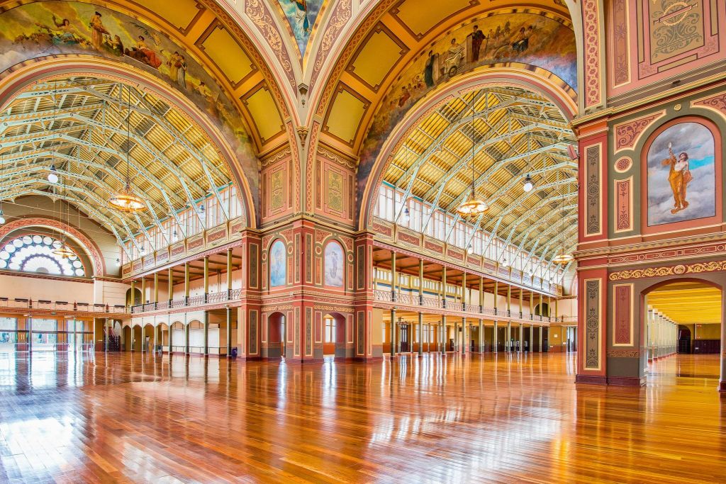 광택이 나는 나무 바닥, 화려한 아치, 벽에 걸린 벽화, 샹들리에가 있는 높고 장식된 천장이 있는 웅장하고 빈 홀입니다.