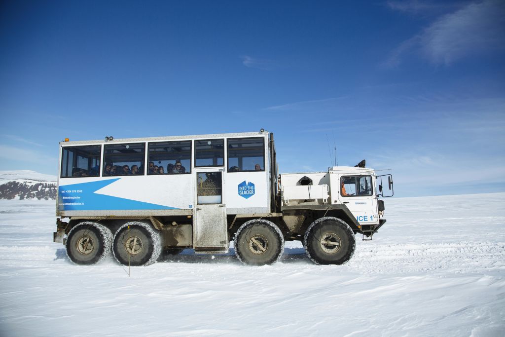 "Into the Glacier" 브랜드가 새겨진 대형 오프로드 차량이 눈을 타고 맑고 푸른 하늘 아래 승객을 실어 나릅니다.