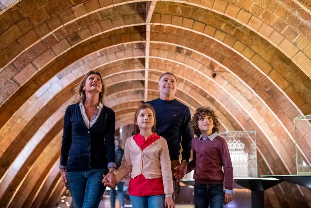 4인 가족이 아치형 천장 아래 서서 위를 바라보고 있습니다. 디스플레이 케이스가 배경에 표시됩니다.