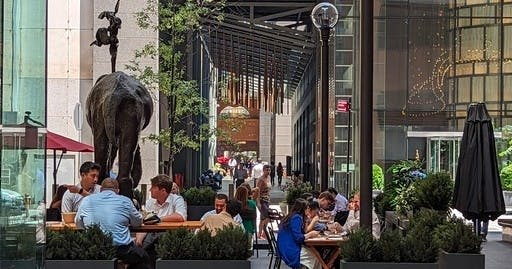 사람들은 코끼리 동상 근처의 테이블에 야외에 앉아 도시를 배경으로 몸통에 균형 잡힌 모습을 하고 있습니다.