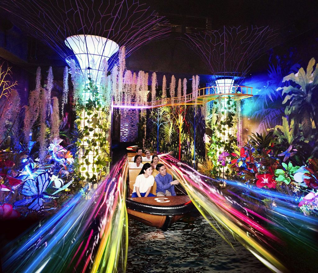 보트를 타는 사람들은 밝은 산책로와 높고 장식적인 기둥이 있는 활기차고 화려하며 빛나는 실내 정원을 지나갑니다.