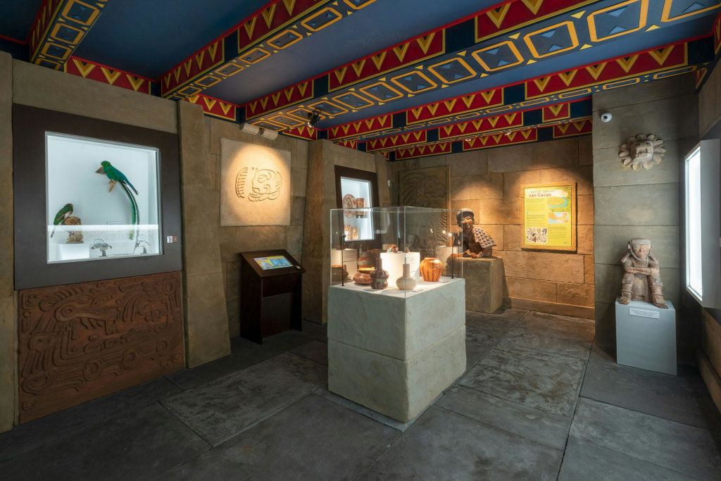 전시 케이스의 고대 유물, 디테일한 벽 조각, 역사적인 복장의 실물 크기의 마네킹이 있는 박물관 전시실.