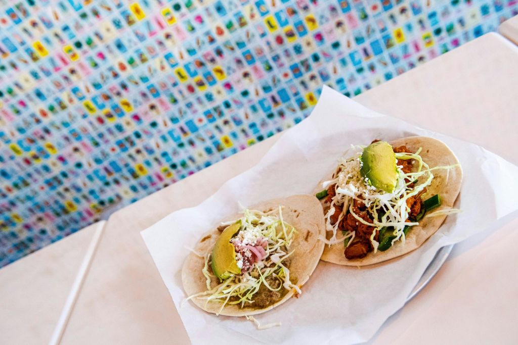 흰색 트레이에 다양한 토핑이 놓인 두 개의 타코가 화려한 타일 배경의 테이블에 놓여 있습니다.