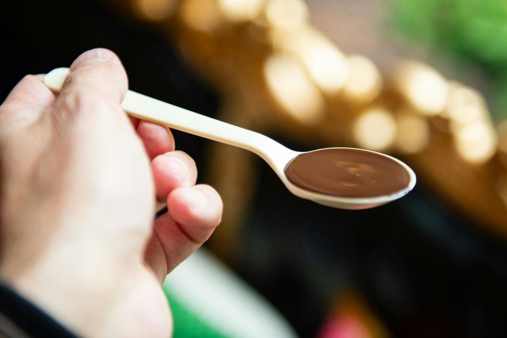 황금색과 녹색 배경이 흐릿한 액체 초콜릿이 담긴 숟가락을 들고 있는 손.