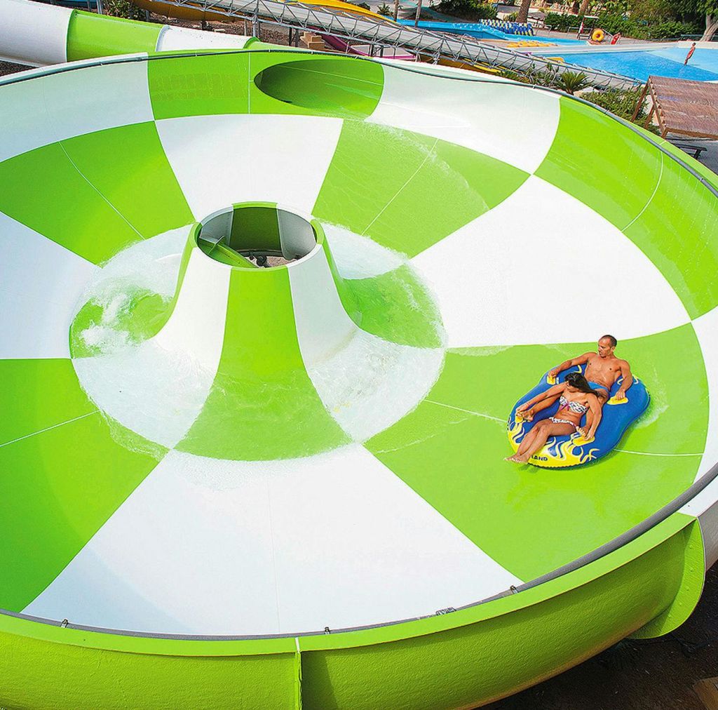 야외 워터파크의 커다란 녹색 및 흰색 물 미끄럼틀에서 팽창식 뗏목을 타는 사람들.